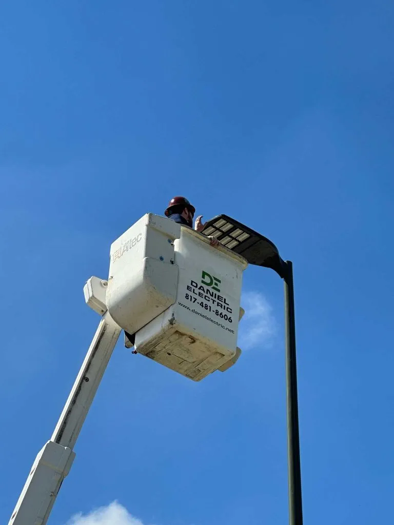 A bucket lift with the DE logo raised to a parking lot light pole