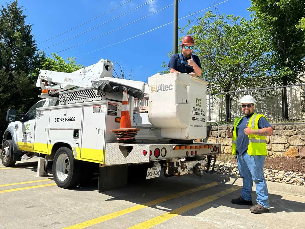 A Daniel Electric bucket truck and two crew members in hard hats working in a parking lot