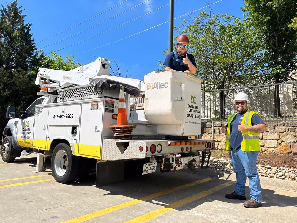 A Daniel Electric bucket truck and two crew members in hard hats working in a parking lot