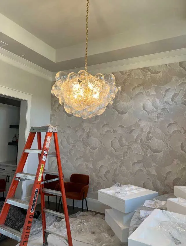 A chandelier hung in a room under finish, with an orange ladder