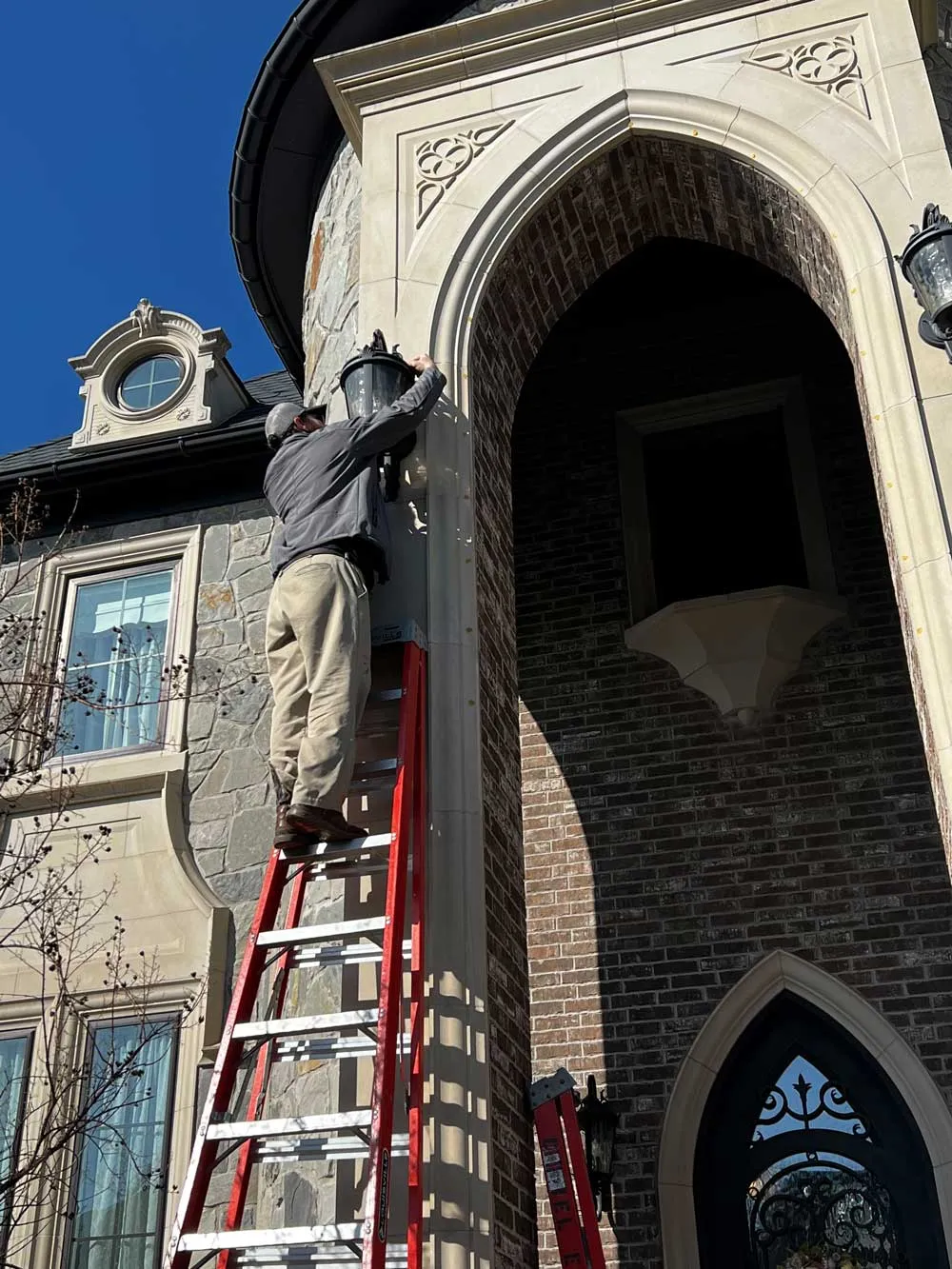 A Daniel Electric electrician on a ladder at the stone arch entry of a home